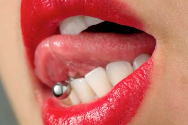 Lèvres rouges mordant la langue percée d’un piercing.