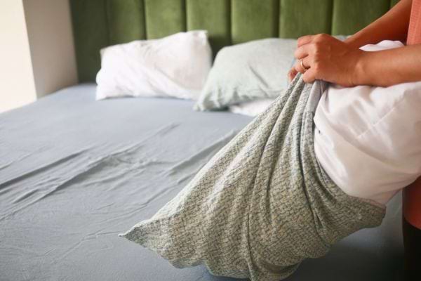 Une personne change une taie verte sur un lit bien fait.