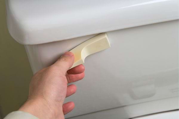 Main appuyant sur la chasse d’eau.