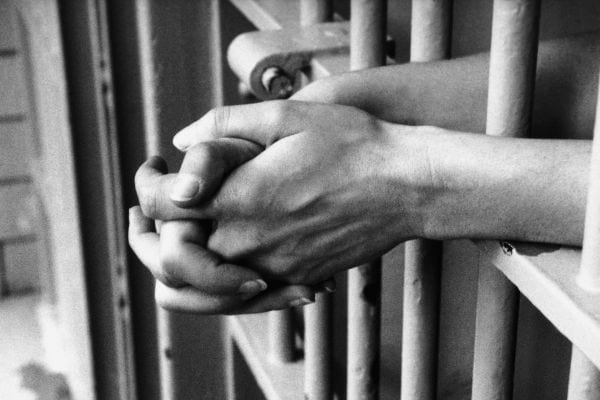 Mains croisées derrière les barreaux d'une cellule.