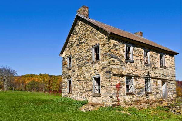 Vieille maison en pierre, abandonnée, dans un champ sous un ciel bleu.