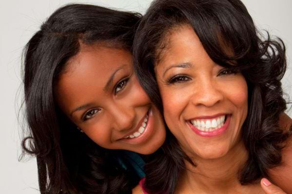 Duo mère-fille souriantes, têtes collées avec complicité.