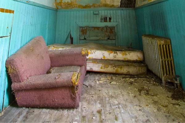 Chambre abandonnée avec canapé et matelas décomposés.