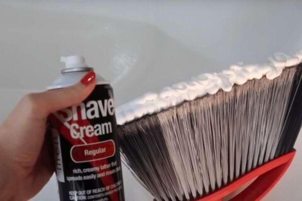 Une main applique de la mousse à raser sur un balai brosse.