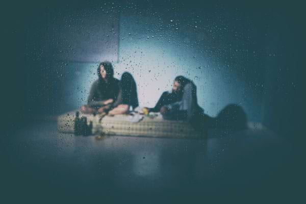 Trois personnes floues assises dans une pièce vue à travers une vitre mouillée.