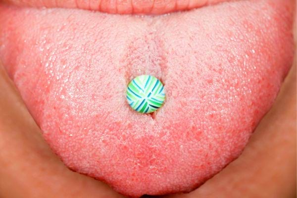 Piercing langue coloré sur langue tirée, motif bleu et vert.