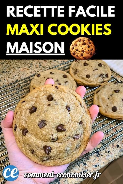 Main tenant un énorme cookie aux pépites de chocolat devant une grille de refroidissement avec d’autres maxi cookies.