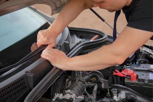 Personne répare un moteur sous le capot d’une voiture.