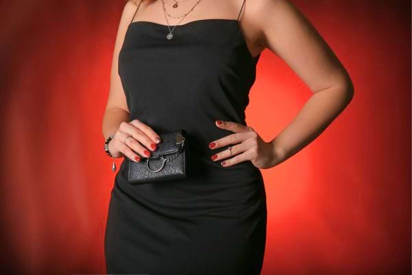 Femme élégante en robe noire tenant une mini pochette.