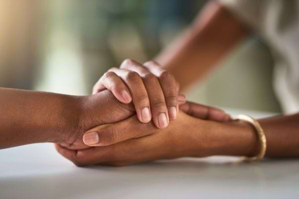 Deux mains entrelacées dans un geste de réconfort.