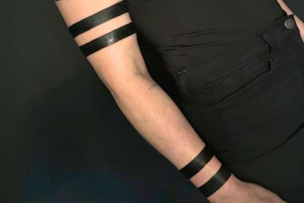 Trois bandes noires épaisses tatouées sur le bras d’une personne en noir.