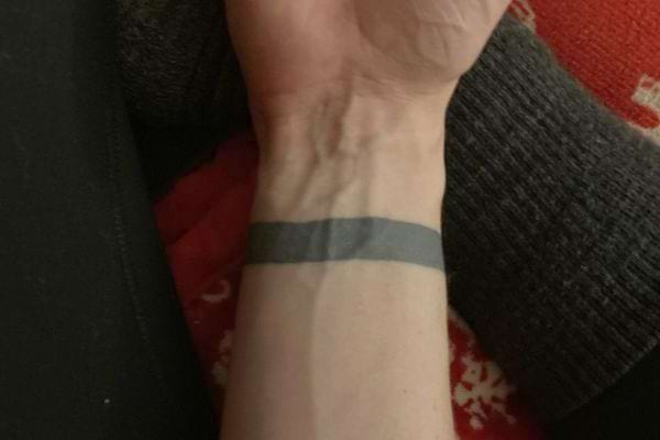 Une fine bande noire tatouée autour du poignet, sur fond rouge.