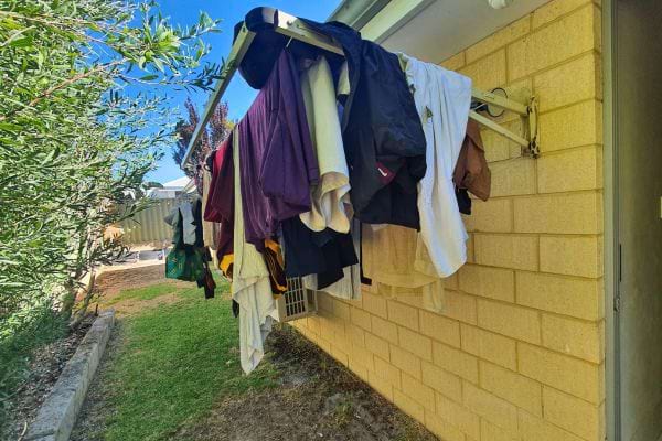Vêtements accrochés à un étendoir mural près d’une maison.