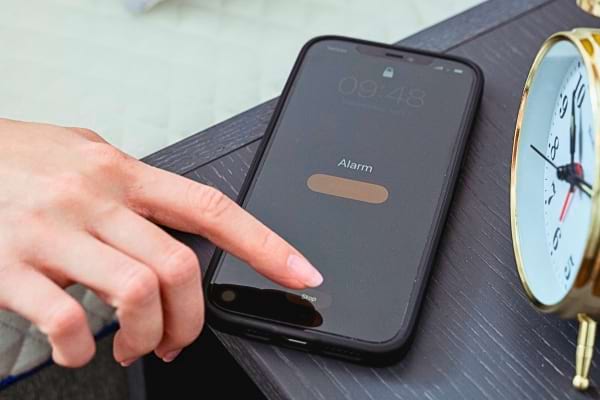 Doigt appuyant sur l’alarme d’un smartphone près d’un réveil.