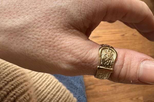Bague dorée décorée portée au pouce gauche.