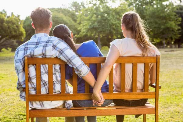 Un homme tient la main d'une autre femme en cachette derrière sa compagne.