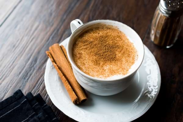 Lait chaud à la cannelle saupoudrée, avec bâtons de cannelle à côté.