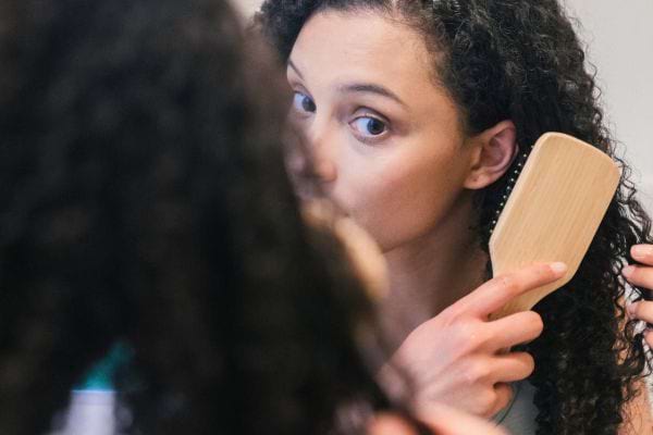 Femme brosse ses boucles devant un miroir.