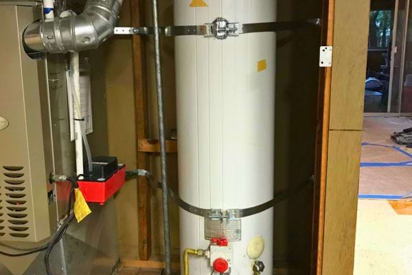 Chauffe-eau vertical fixé avec des sangles métalliques.