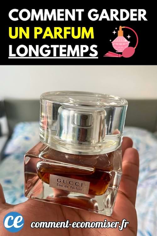 Un flacon de parfum Gucci transparent à moitié rempli, tenu dans une main devant un lit.