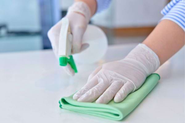 Mains nettoyant une surface avec un spray.