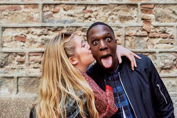 Une femme embrasse la joue d’un homme qui fait une grimace drôle.