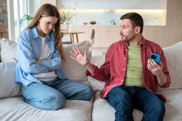 Une femme contrariée confronte son compagnon qui se justifie avec son téléphone.