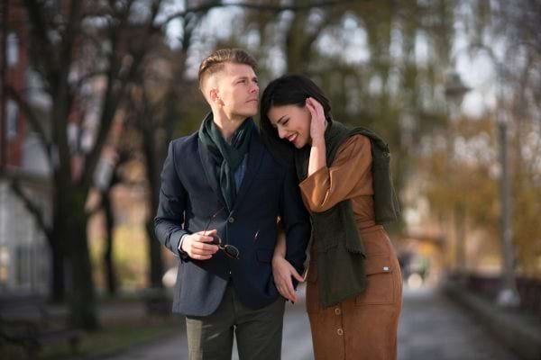 Un couple élégant partage un moment complice dans une allée arborée.