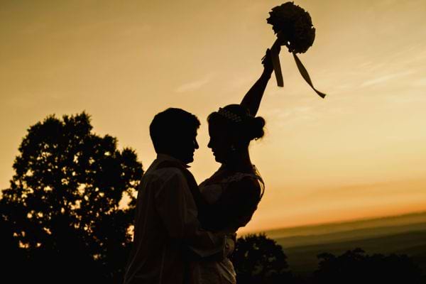 Couple de mariés en silhouette au coucher du soleil.
