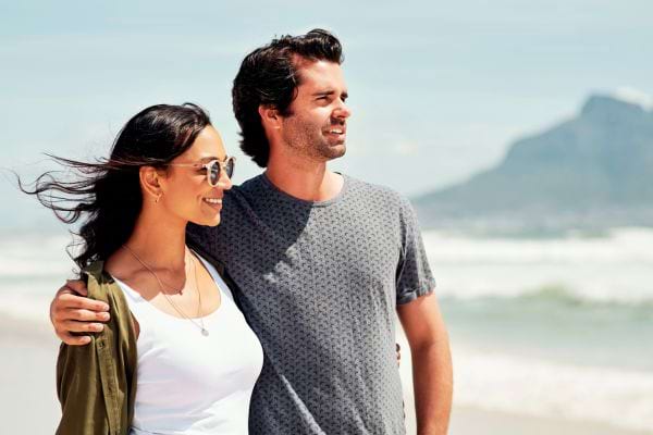 Un couple marche enlacé au bord de la mer, regardant l’horizon.