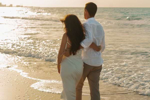 Un couple marche enlacé sur la plage au coucher du soleil.