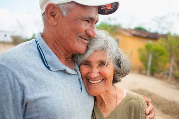 Deux retraités s’enlacent en souriant à l’extérieur.