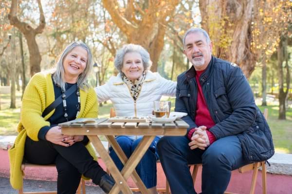 Trois seniors souriants assis à une table en extérieur.