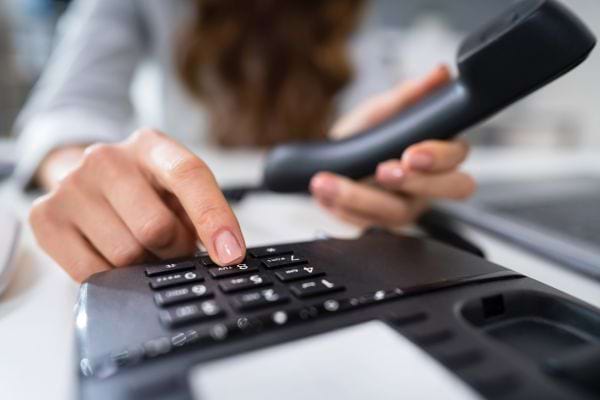 Femme composant un numéro sur un téléphone fixe.
