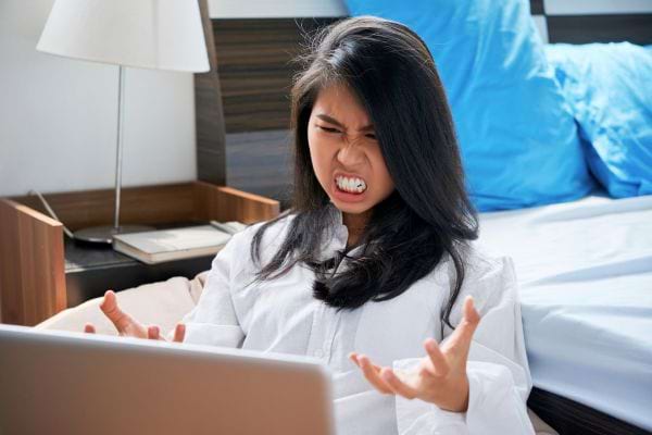 Femme en colère devant un ordinateur, visiblement irritée.