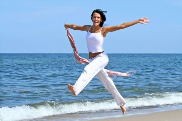 Femme souriante sautant sur la plage.