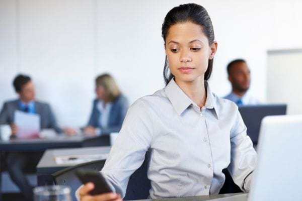 Une femme regarde discrètement son téléphone au travail.