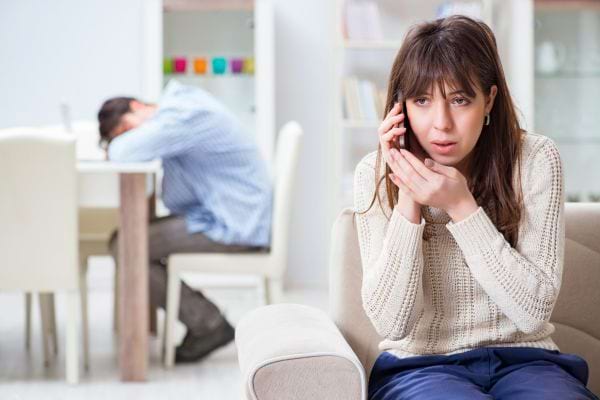 Une femme appelle en secret, l’homme derrière semble abattu.