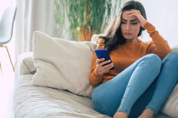 Une femme stressée lit un message sur son canapé.