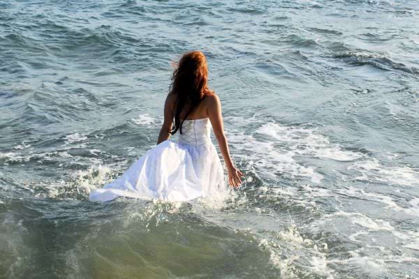 Femme en robe blanche marchant dans les vagues.