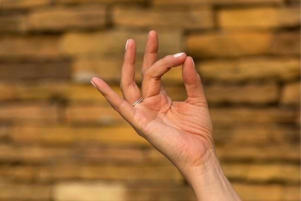 Main levée en mudra devant un mur en pierre.