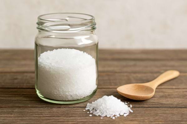 Bocal rempli de gros sel blanc et cuillère en bois à côté.
