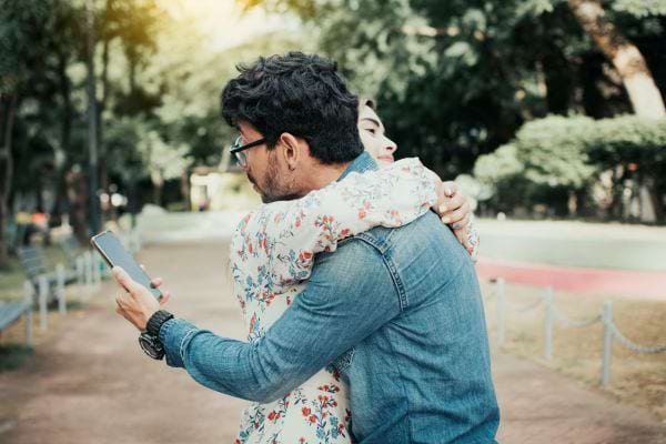 Un homme enlace une femme tout en regardant son téléphone.