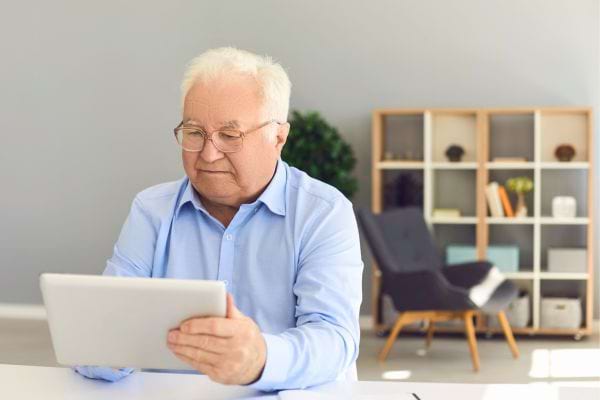 Un retraité consulte une tablette assis à son bureau.