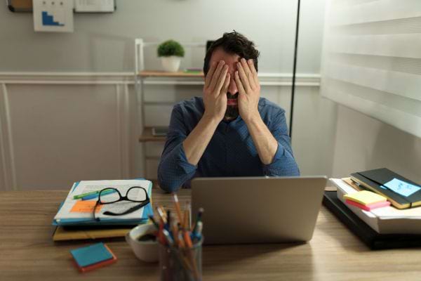 Homme stressé, mains sur le visage, devant son ordinateur.