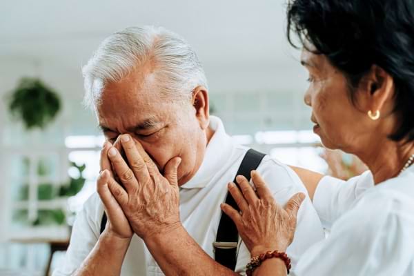 Homme âgé en détresse, soutenu par une femme inquiète.