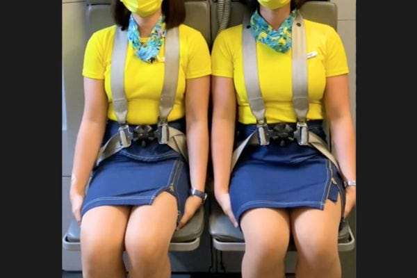 Deux h&ocirc;tesses assises c&ocirc;te &agrave; c&ocirc;te, ceintur&eacute;es, en uniforme jaune et bleu.