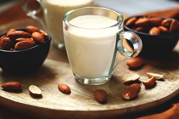 Verre de lait d’amande posé sur un plateau avec des amandes entières.