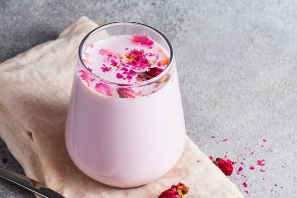 Lait rosé décoré de pétales de fleurs dans un verre transparent.