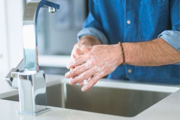 Homme se lave soigneusement les mains au savon sous l’eau courante.